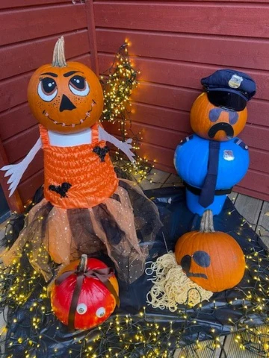 En pumpa-dam med pliriga &ouml;gon och orange kl&auml;nning st&aring;r bredvid en polis gjord av en pumpa, med uniform, slips och hatt.