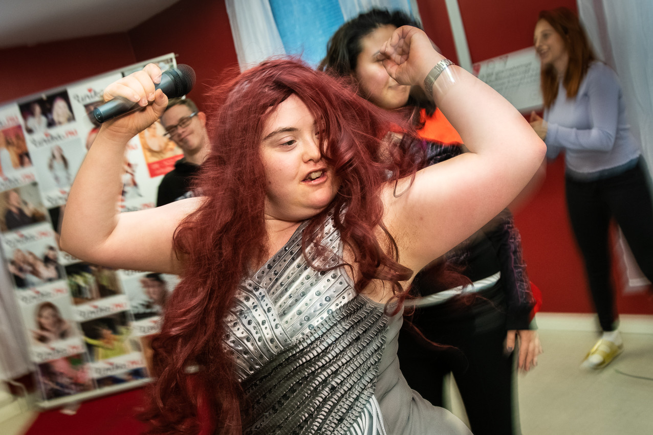 deltagare på unikas dagliga verksamhet med mikrofon i handen och glittrande klänning på sig.