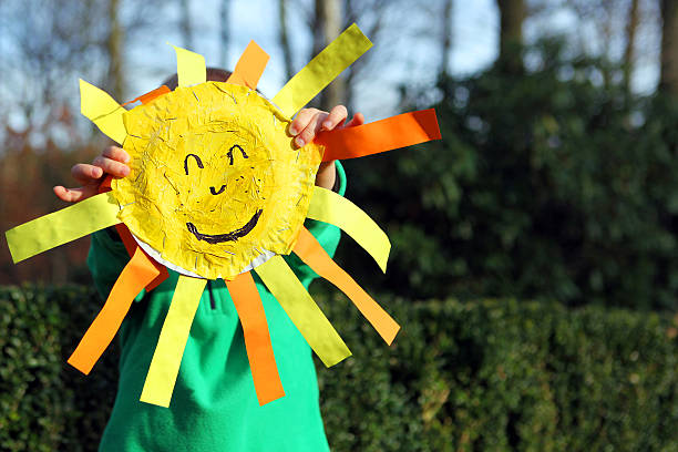 Barn gömmer sig bakom och håller upp en egenhändigt pysslad sol