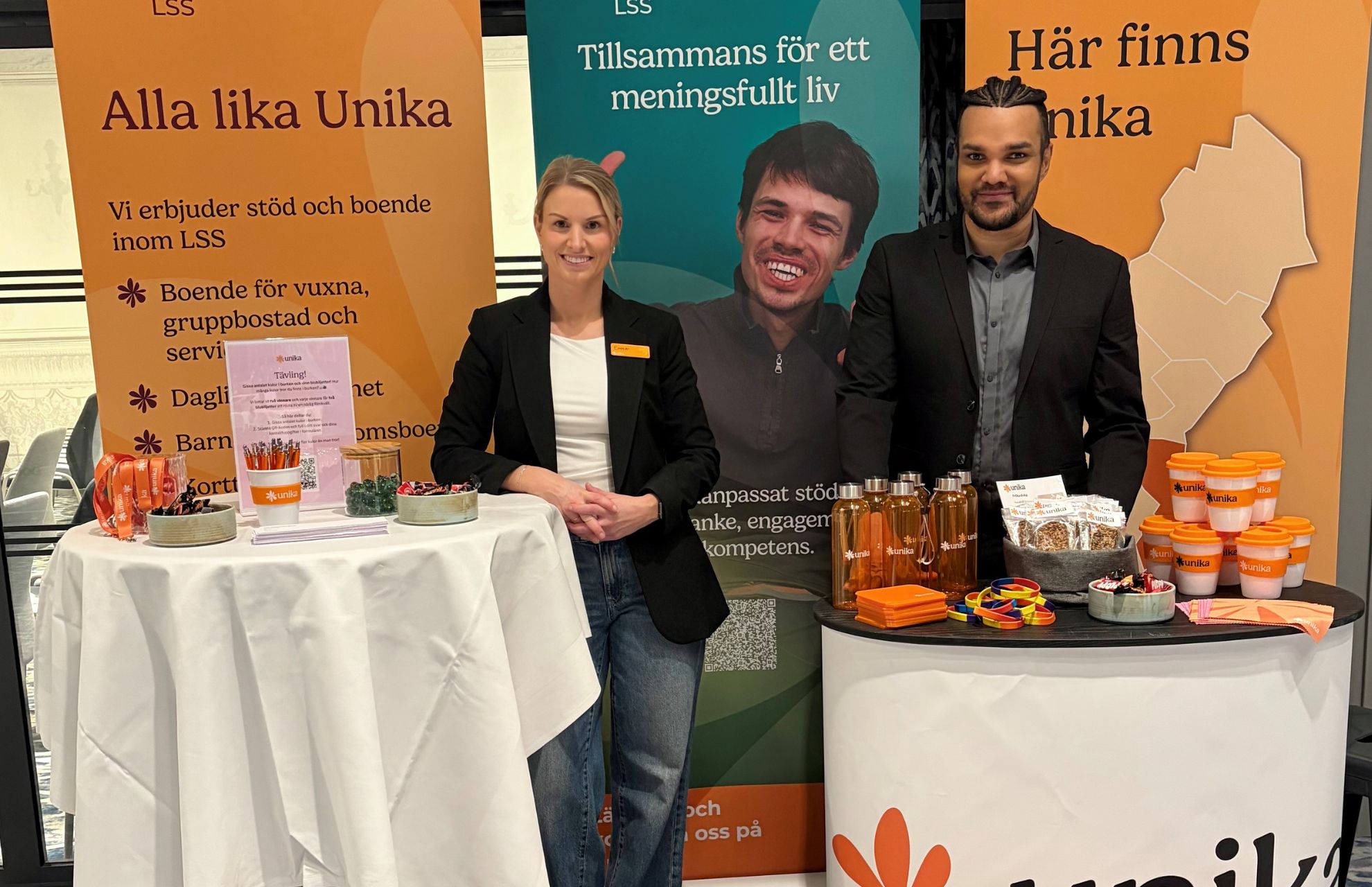 Två representanter från Unika vid ett tidigare event, i en monter med Unikas budskap "Alla lika unika".